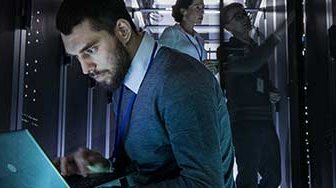 Businessman on laptop in large server room