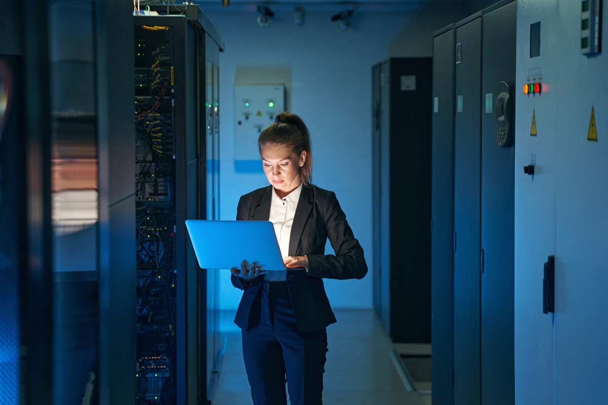 young woman using a laptop while working in a server room