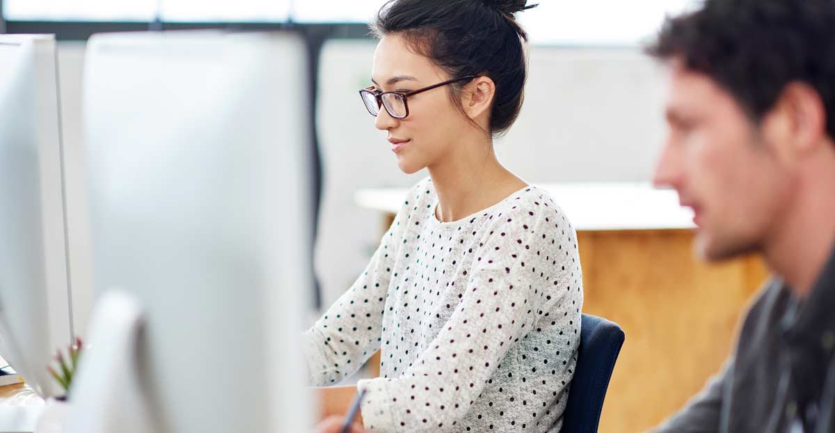Young woman looking at iMac next to coworker